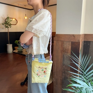 Détail du sac seau en toile jaune avec broderie florale et bandoulière en corde tressée
