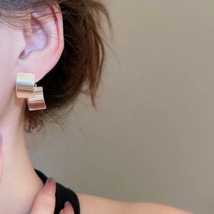 Close-up of square polished metal earrings with silver finish in a minimalist layered design