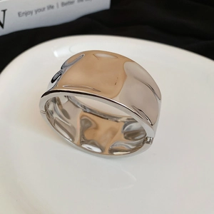 Polished silver irregular geometric wide metal bangle with hinge on a ceramic plate