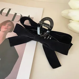 Detail of a large black velvet bow hair claw clip placed on a fashion magazine with flowers