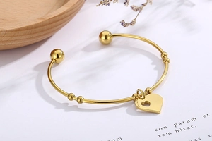 Detailed view of an elegant gold heart charm open bangle on a white card background