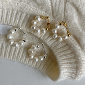 Detailed shot of pearl C-shaped earrings in gold and silver on white knit fabric