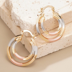 Three-tone layered metal hoop earrings in gold silver and rose gold on a stone background