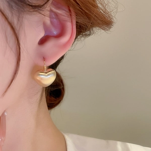 Close-up of a model wearing a brushed gold heart-shaped earring with a vintage hook design