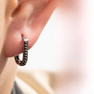 Close-up of a silver V-shaped earring with twisted rope texture worn on the earlobe