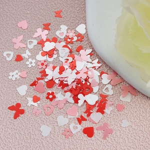 Detailed shot of pink, white, and red heart and butterfly nail art sequins on textured background