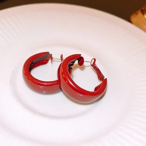 Detail of chunky deep red enamel hoop earrings on a minimalist white ceramic tray