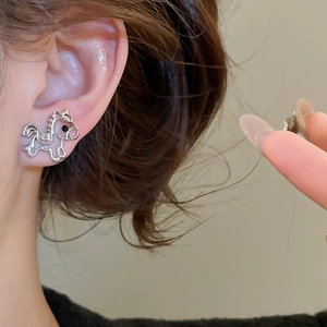 Close-up of a silver hollow horse pendant earring worn on a model's ear in a daily setting