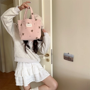 Model holding a pink corduroy handbag featuring cute embroidered bears in a soft room