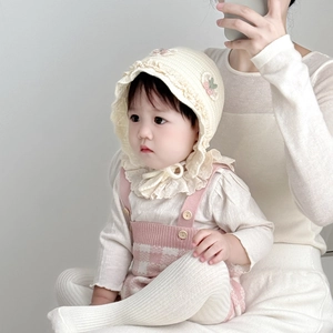 Detail of cream baby ear-flap hat with lace trim and soft knitted cotton texture