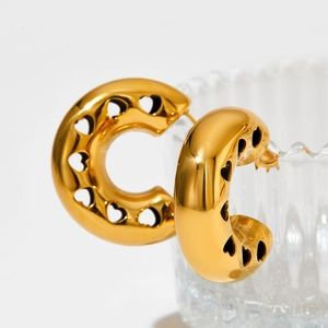 Polished gold C-shape hoop earrings with hollow heart patterns on glass background