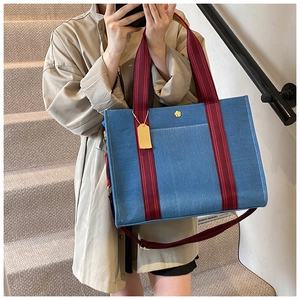 Detail of blue denim tote featuring red striped handles and a gold plum blossom logo