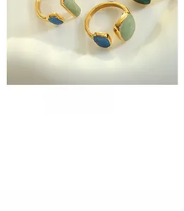 Detail view of gold titanium earrings with green and blue enamel on a white tray
