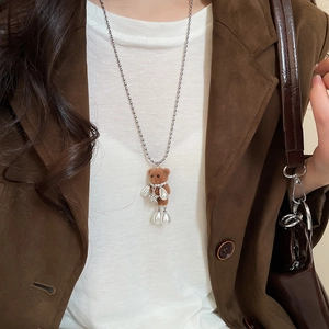 Detailed view of flocked bear and pearl pendant necklace on a model wearing a suede jacket