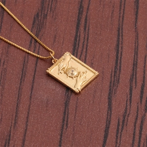 Gros plan du pendentif rectangulaire doré avec gravure œil du soleil et mains