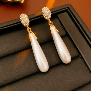Detailed shot of golden teardrop pearl earrings with pavé diamonds in a display box
