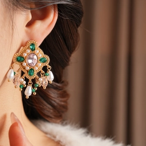 Gros plan de boucles d'oreilles vintage en or avec pierres d'émeraude et perles sur modèle