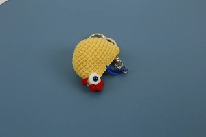 Macro shot of handmade yellow crochet chicken keychain with red comb and blue lanyard