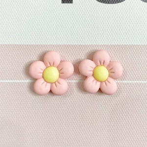 Close-up of pink resin five-petal flower earrings with yellow centers on textured fabric