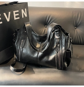 Detail view of large black tote bag with vintage rivets and side pockets on a dark bench