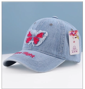 Detail of light blue denim baseball cap featuring red butterfly and free flight embroidery