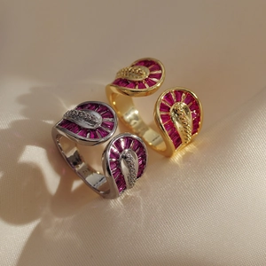 Close-up of gold and silver double-layered snake rings with red zircon on beige silk