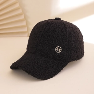 Detailed side view of thick black lamb wool baseball cap with gold metal M logo badge