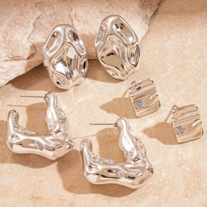 Macro detail of silver geometric earrings set with lava texture on marble background