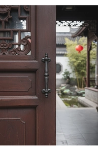 Detail view of retro black iron door handle with hammer texture on carved wood door