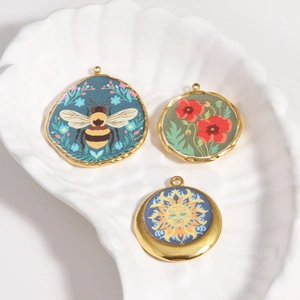 Close-up of DIY jewelry pendants with bee and floral motifs on a white shell tray