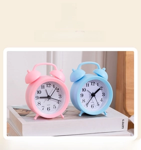Close-up of small retro quartz alarm clocks in pink and blue on a stack of books