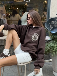 Brown half-zip sweatshirt with small logo on chest shown in a street style setting