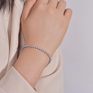 Detail view of a silver tennis bracelet with round white zircons worn on a female wrist