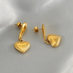 Macro view of gold heart drop earrings with radial engraved texture on satin fabric