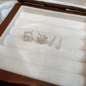 Close-up of four-piece earring set with silver snowflake studs and pearl studs on velvet
