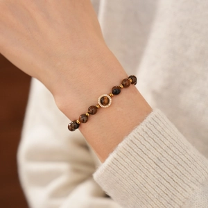 Bracelet en perles d'oeil de tigre avec détails dorés porté sur une manche en tricot