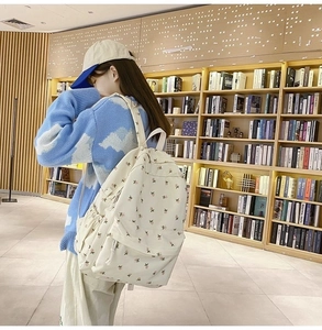 Side view of a floral embroidered canvas backpack in cream white for students