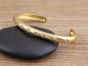 Detail of 18k gold plated C-shape open bracelet with oval marquise-cut white zircons