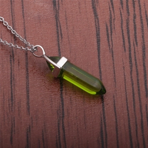 Macro shot of green hexagonal crystal pendant on silver chain over dark wood background