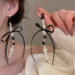 Detail of long pearl tassel earrings with black ribbon bow on golden stud earring