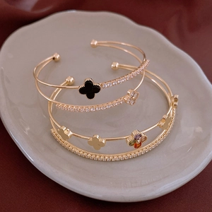 Macro detail of gold-plated double-layer clover bangles with zircon inlay on ceramic tray