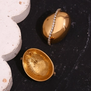 Macro shot of 18K gold plated oval earrings with white zircon inlay on black marble