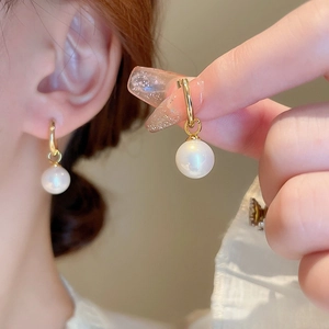 Détail de créoles dorées avec perles blanches sur modèle et gros plan à la main
