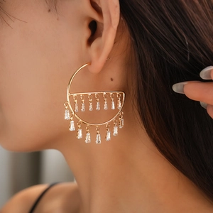 Close-up of gold geometric hoop earrings with dangling zircon fringe on a female model