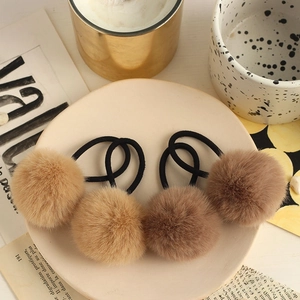 Detail of plush faux fur pom pom hair ties in brown tones displayed on a ceramic plate