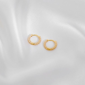 Close-up of golden hoop earrings with white spiral texture on silky white fabric