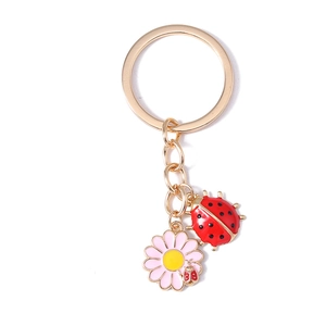 Pastel pink daisy and red ladybug keychain with golden metal finish on white background