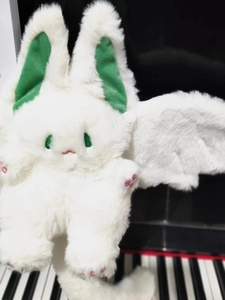 Detail of white bat rabbit plush with green ears and wings on a piano keyboard background