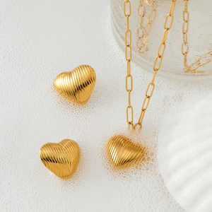Textured gold heart pendant necklace and earring set on white foam with water drops