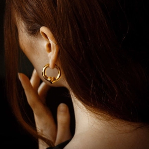 Chic 18K two-tone gold heart hoop earrings on a model with an artistic dark background